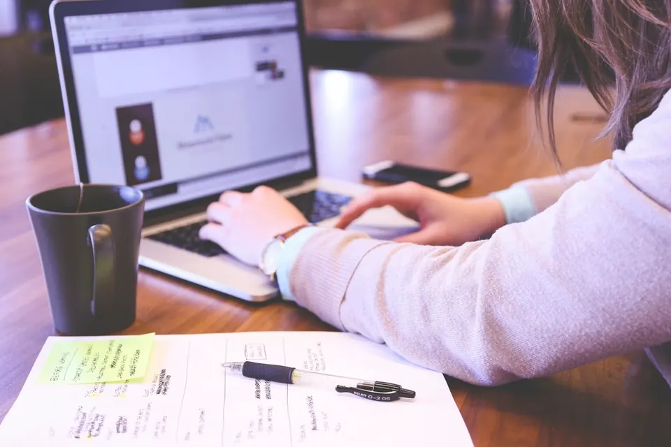 Une personne travaille sur un ordinateur portable, des formulaires posés à côté d'elle